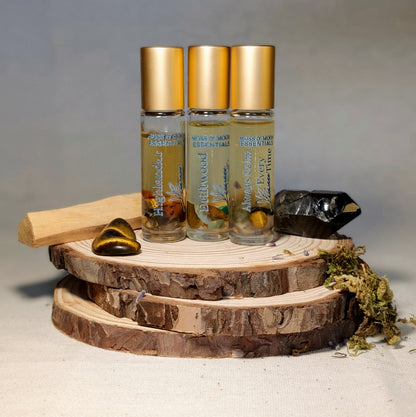 Three essential oil bottles with gold caps on a wooden surface with crystals and herbs.