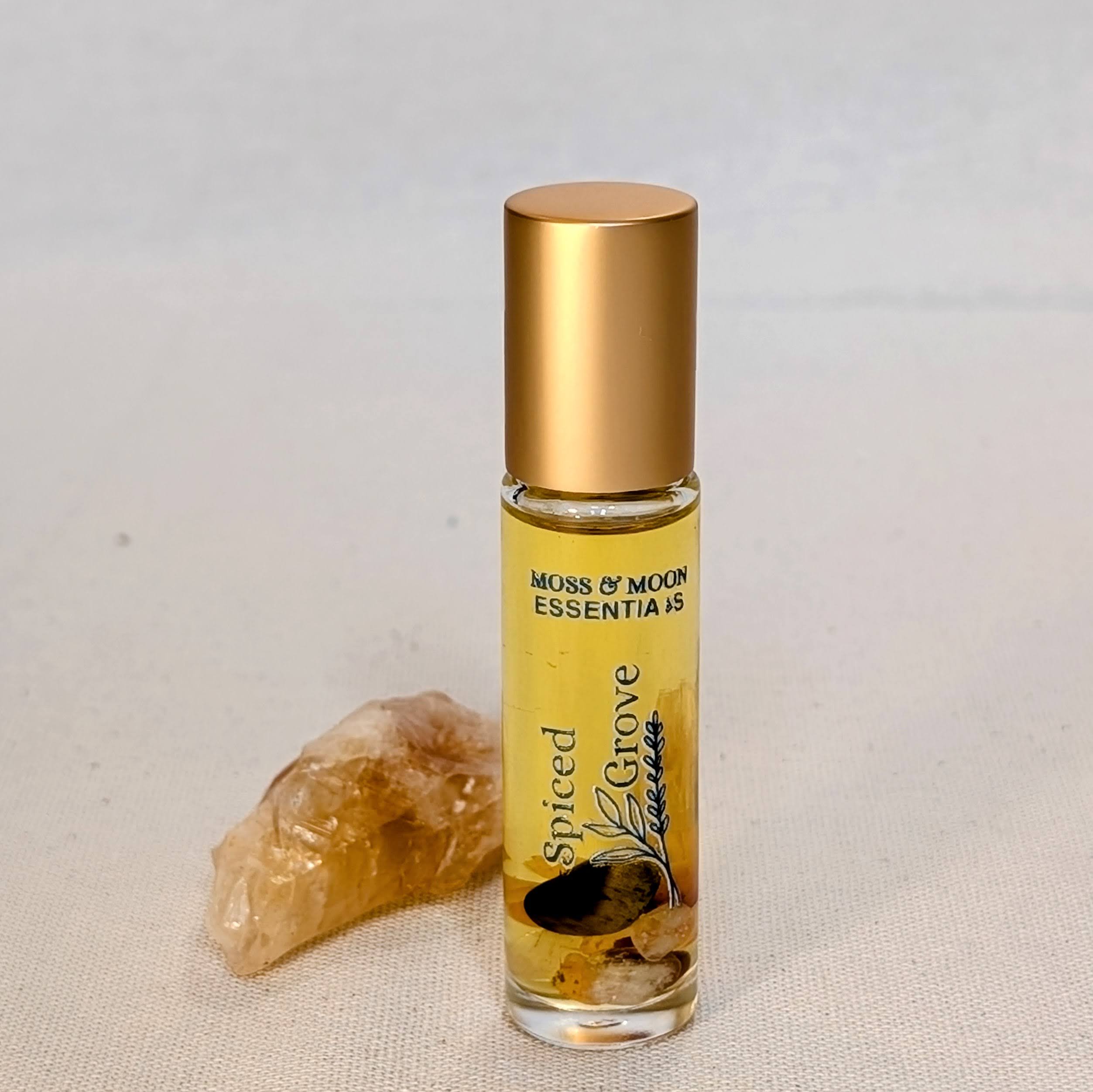 Roll-on bottle of 'Spiced Grove' by Moss & Moon Essentia on a textured surface with a beige stone.