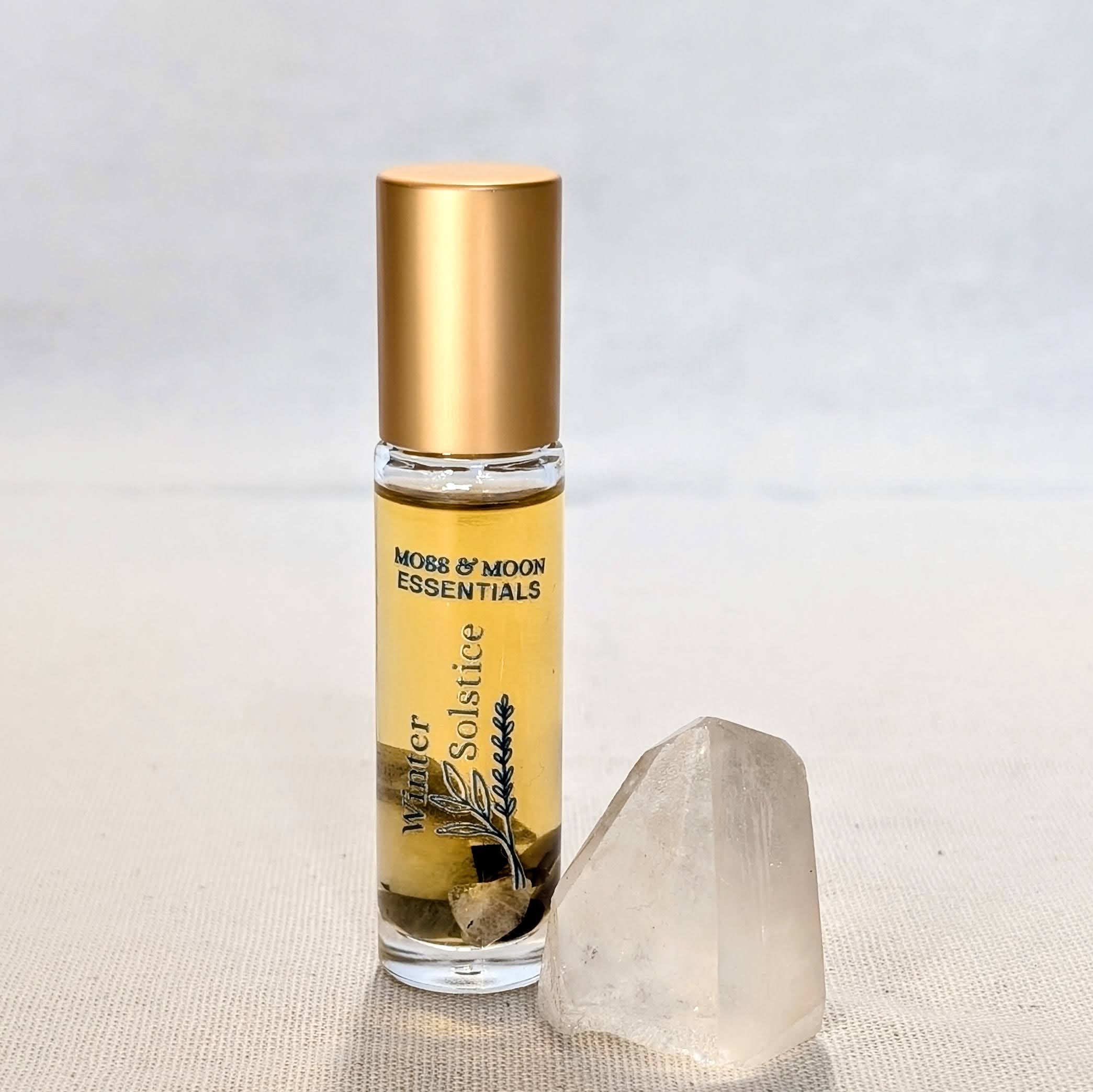 Roll-on bottle of 'Winter Solstice' essential oil by Moss & Moon Essentials on a textured surface with a crystal.